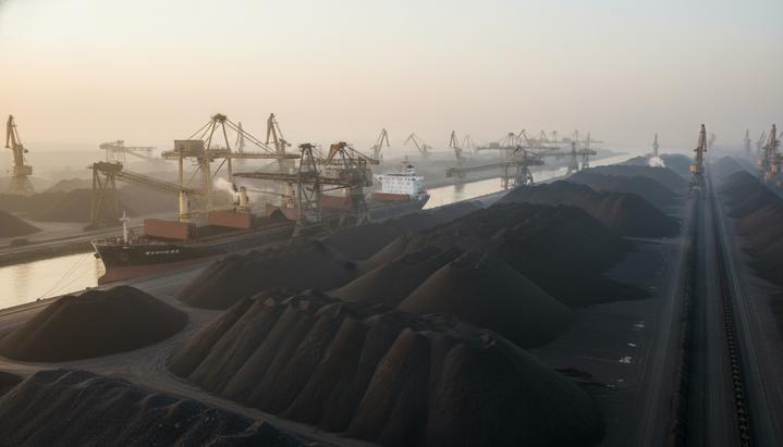 Огромный склад угля в порту Циньхуандао, Китай. Портовые краны загружают уголь на пришвартованное грузовое судно.